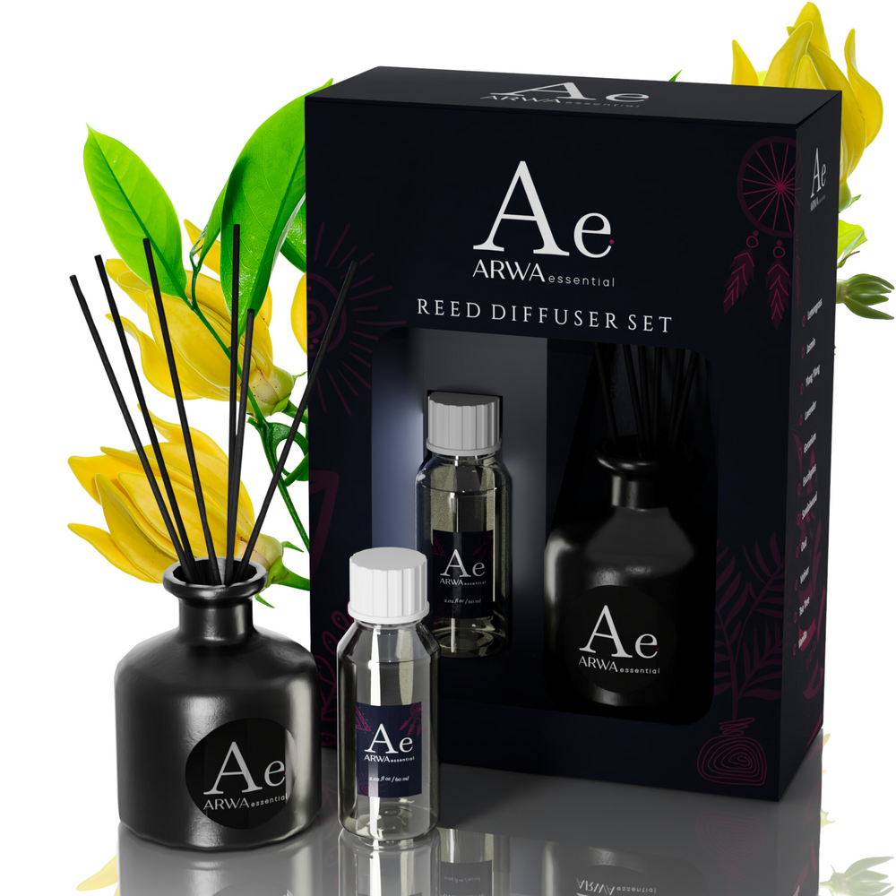 ARWA Essential Ylang-Ylang Reed Diffuser Set - black ceramic diffuser pot with reed sticks, fragrance oil bottle and refill bottle with packaging box, yellow ylang-ylang flowers in background