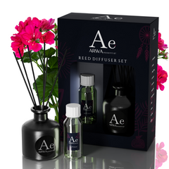 ARWA Essential Geranium Reed Diffuser Set - black ceramic diffuser pot with reed sticks, fragrance oil bottle and refill bottle with packaging box, pink geranium flowers in background